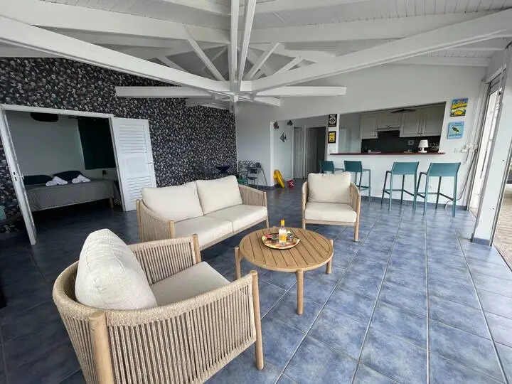 Salon moderne et lumineux avec canapé, fauteuils et cuisine équipée ouverte - Appartement Grand Large Trois Îlets Martinique