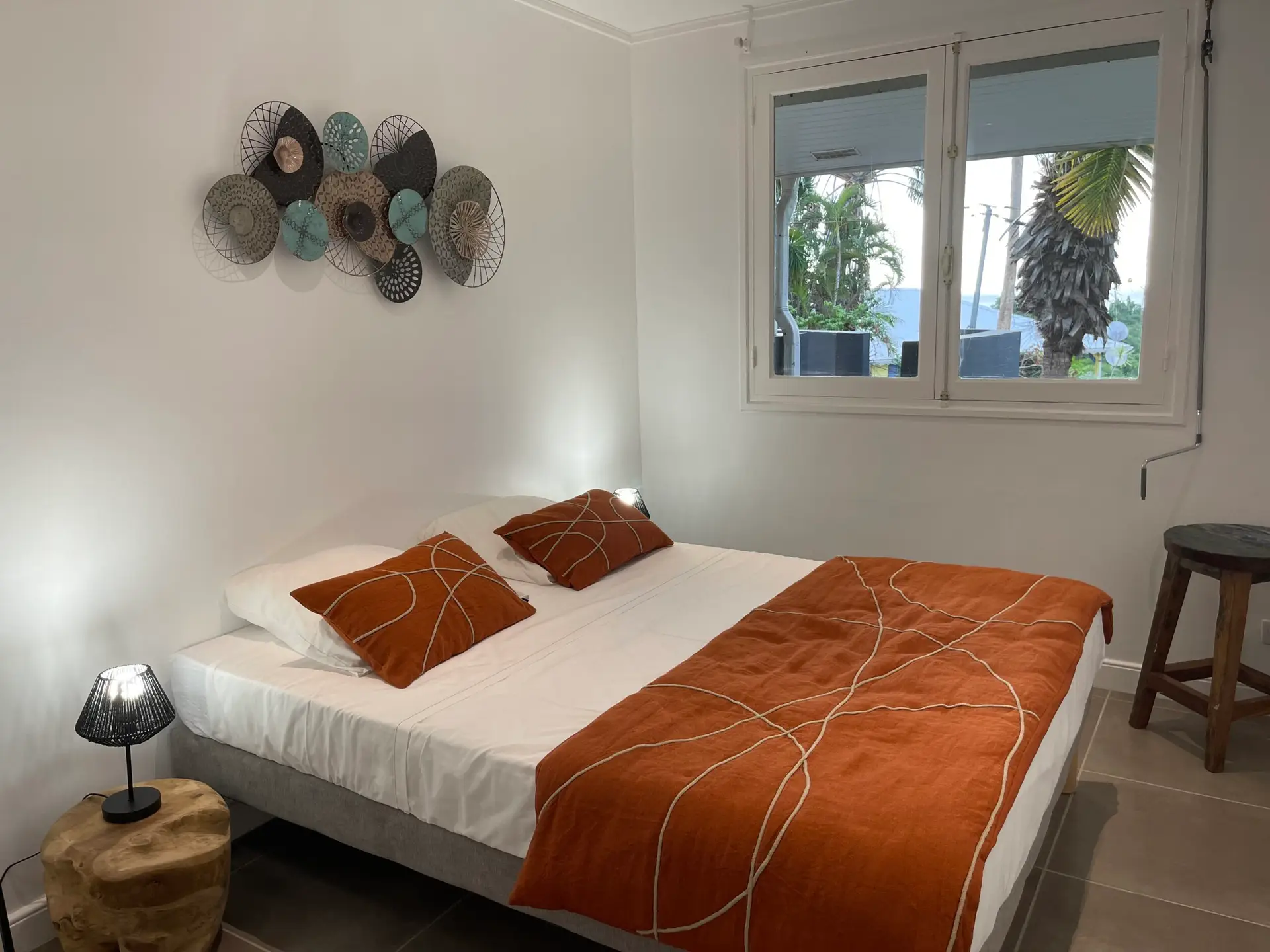 Chambre double de la villa Héliconia en Martinique, avec décoration naturelle, parure orange, luminaires modernes et vue sur le jardin tropical.