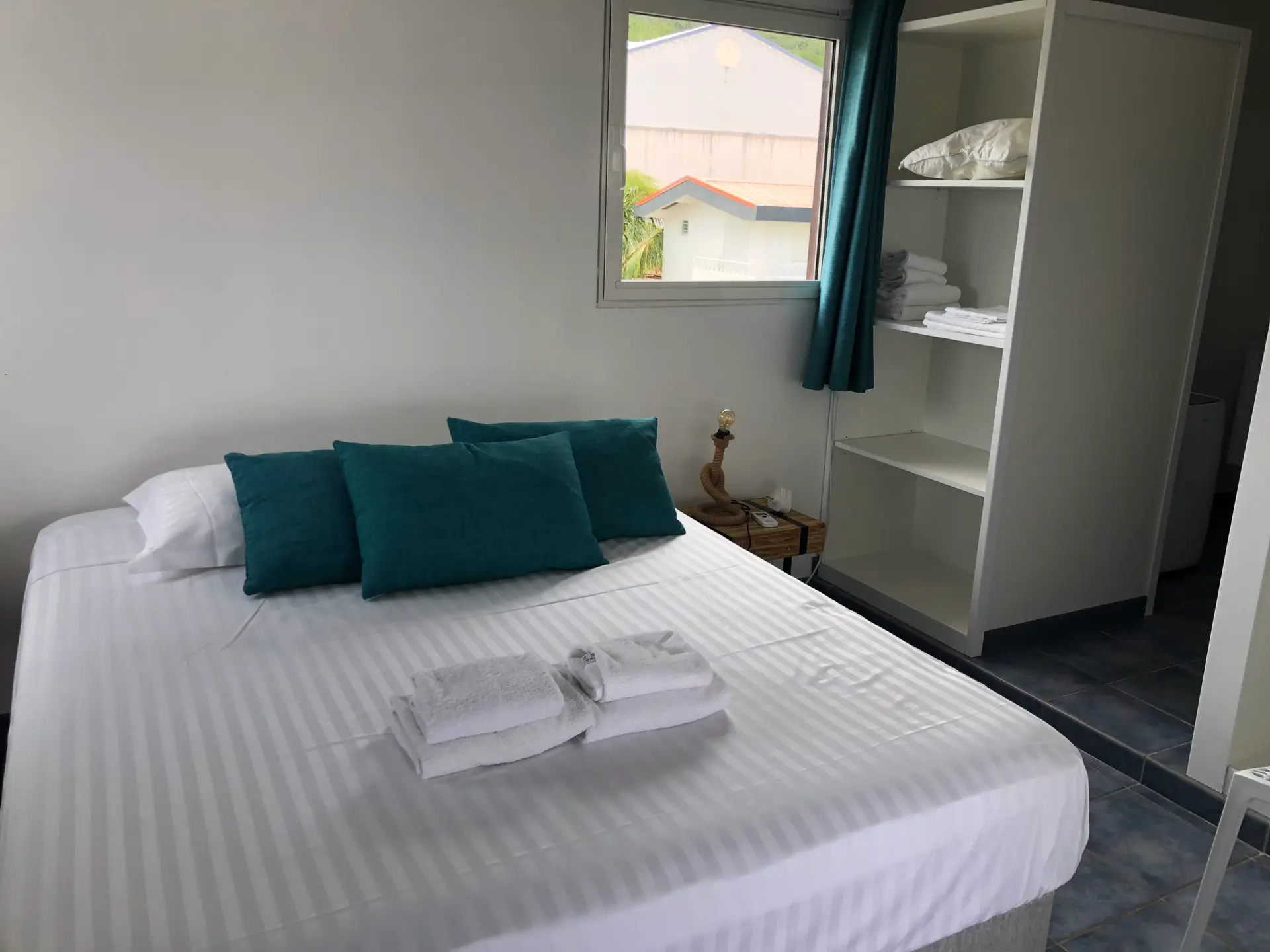 Chambre de l’appartement Grand Large en Martinique, avec un grand lit, linge propre et espace de rangement ouvert.