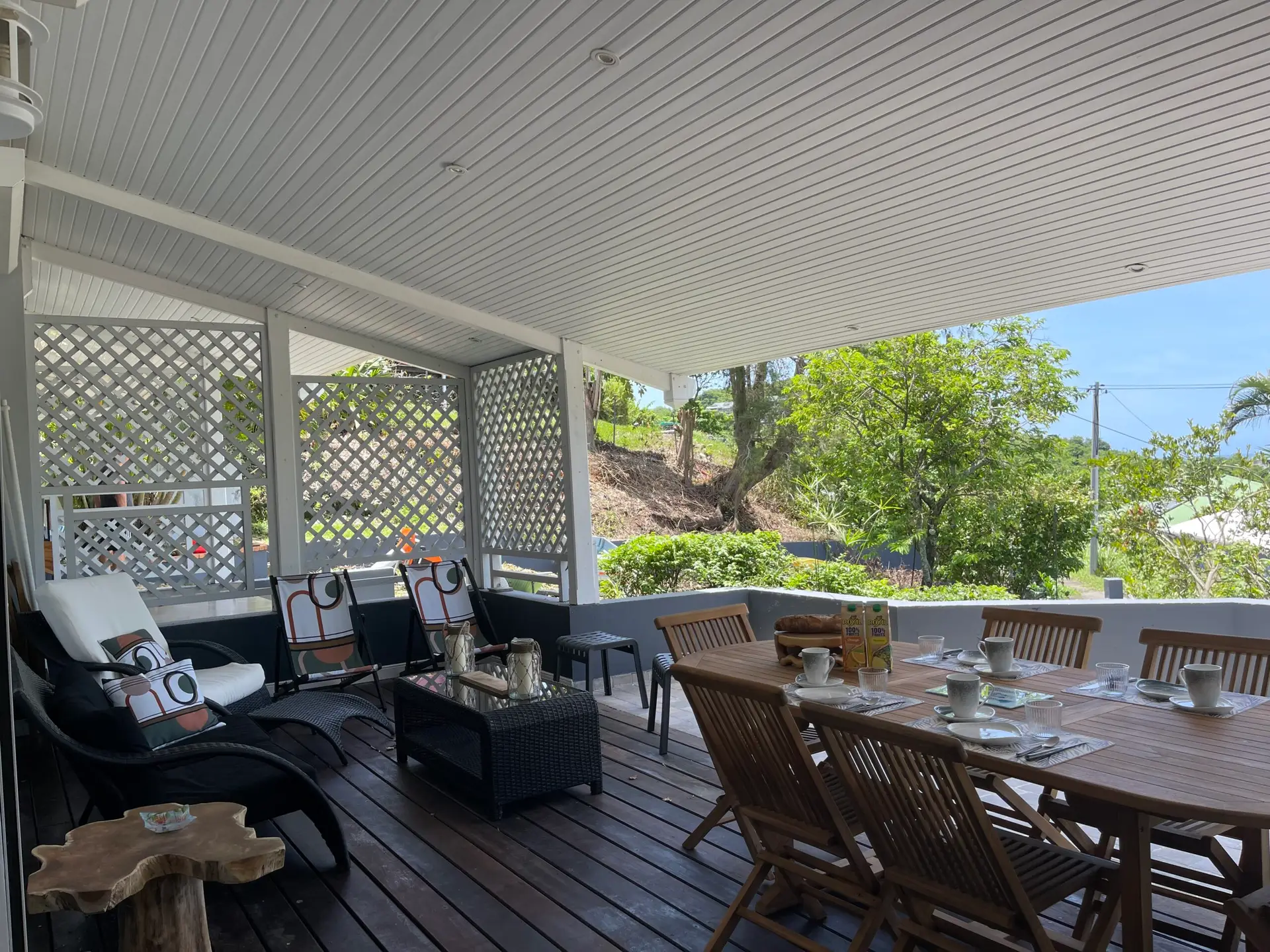 Grande terrasse de la villa Héliconia en Martinique, aménagée avec un espace repas et un salon extérieur donnant sur un jardin tropical.